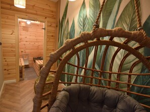 Een houten interieur met een rieten stoel, een bank en een muurschildering van bladeren.