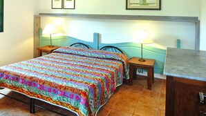 Un lit recouvert d’une couverture aux couleurs vives, deux lampes de chevet et une petite table de nuit en bois.