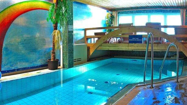 An indoor swimming pool with a tiled floor, a wooden deck area, and a sign indicating a height of 1.4 meters.