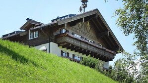 A traditional chalet with a sloped roof, wooden balconies, and a weather vane on the roof.