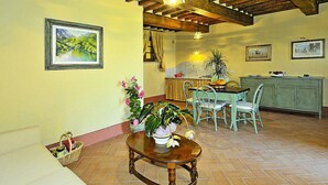 A dining area with a wooden table and chairs, a kitchen in the background, and a ceiling with exposed beams. - Estate in Monte Serra With Pool & Olive Trees (Buti)
