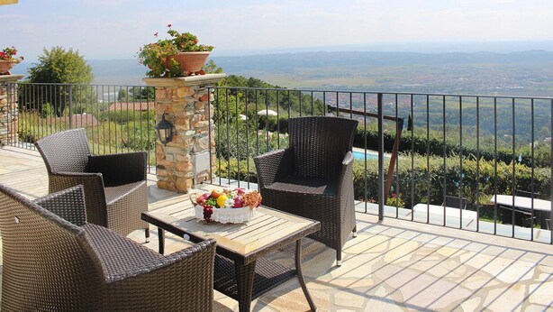 A patio with wicker furniture, a stone pillar, and a table with fruit. - Estate in Monte Serra With Pool & Olive Trees (Buti)