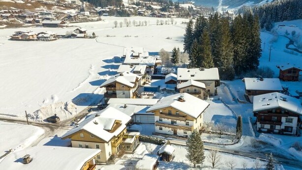 Un villaggio innevato con case in legno tradizionali, cielo sereno e montagne sullo sfondo.