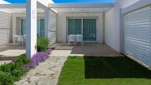 A modern outdoor patio with a stone pathway, a grassy area, and a seating arrangement with white chairs. - Residence Capo Falcone, Stintino (Stintino)