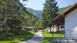 A rural road leading to a row of traditional wooden houses with sloped roofs, surrounded by lush greenery and mountains in the background. - Apartment Santa Lucia in Bezecca (Ledro)