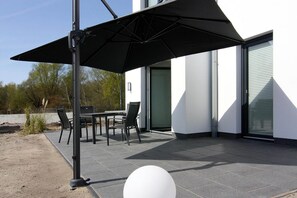 An outdoor patio with a table and chairs, a black umbrella, and a white spherical object on the ground. - Haustierfreundlicher Aufenthalt am Yachthafen (Peenemünde)