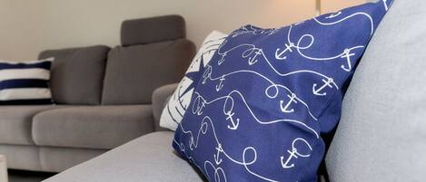 A grey sofa with a blue pillow featuring white anchor patterns.