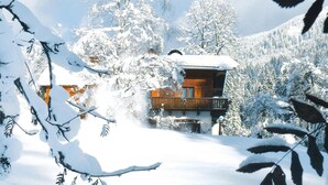 A wooden cabin with a balcony, surrounded by snow-covered trees and a mountainous backdrop. - Apartment in Huttau Near Ski Amade Slopes (Huettau)