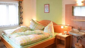 A bedroom with a bed, bedside table, lamp, and a bathroom with a sink and mirror. - Apartment in Huttau Near Ski Amade Slopes (Huettau)