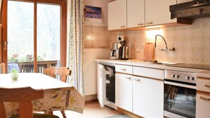 A kitchen with white cabinets, a built-in oven, a coffee maker, and a window with a view of greenery. - Apartment in Huttau Near Ski Amade Slopes (Huettau)