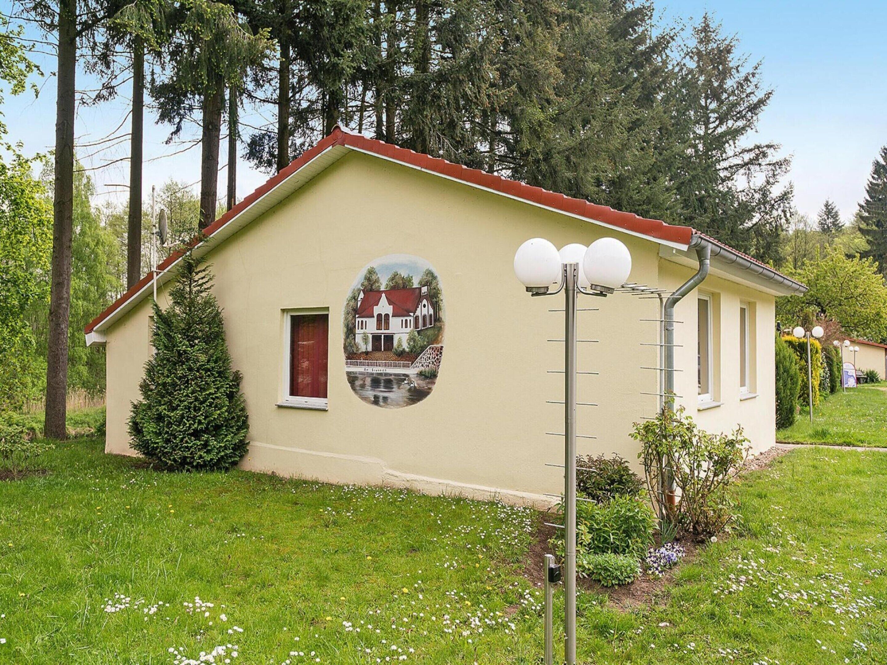 Um edifício térreo com telhado vermelho, uma pequena janela e porta vermelha, e um mural circular de uma casa na parede.