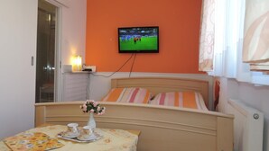 A bedroom with a bed, a table with a floral tablecloth, two cups, and a vase with flowers. A TV is mounted on the wall above the bed. - Holiday Home Dziwnowek by Clean Beach (Dziwnów)