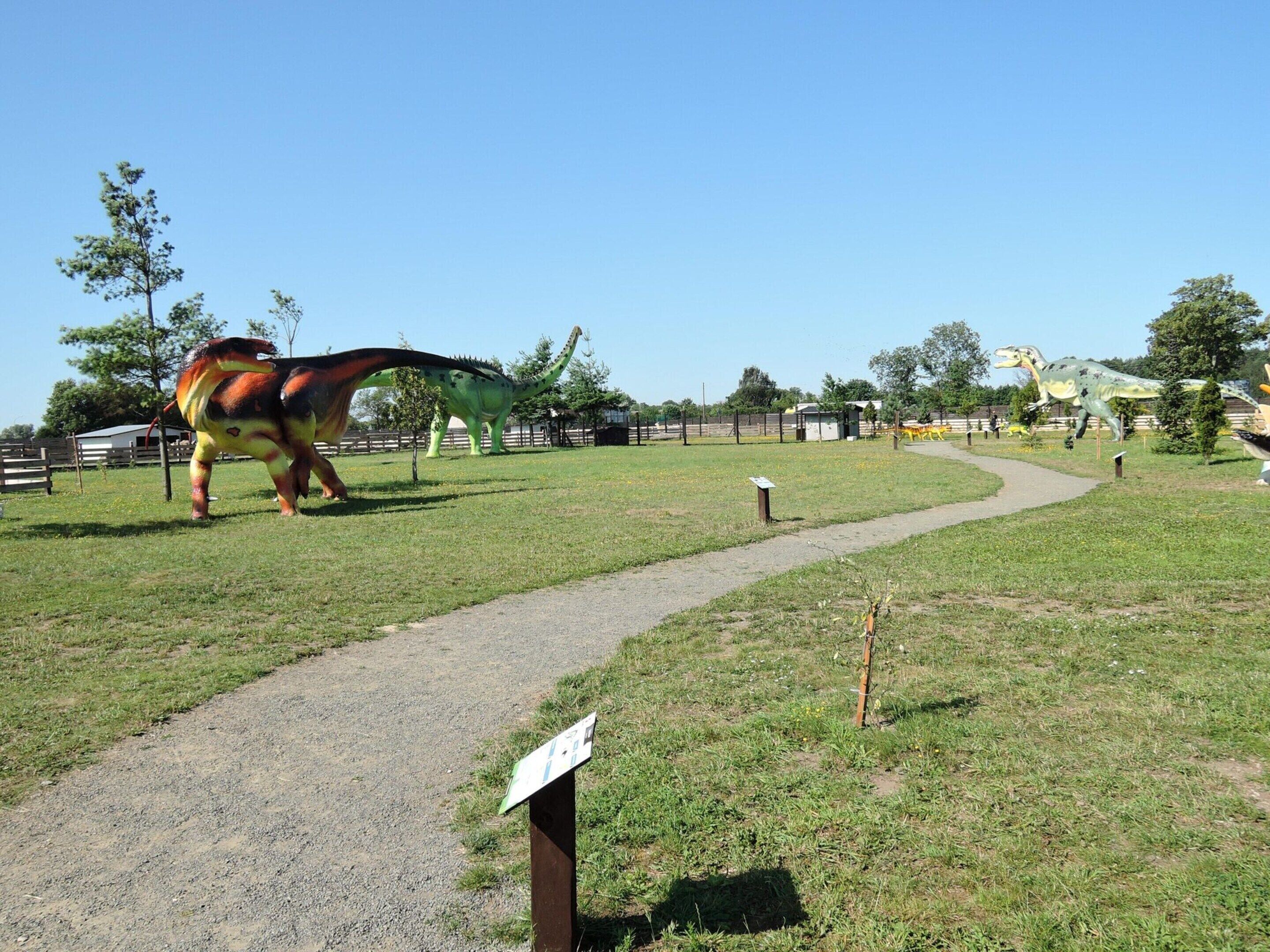 Eine Dinosaurierausstellung in einem Park mit Kiesweg und Umzäunung.