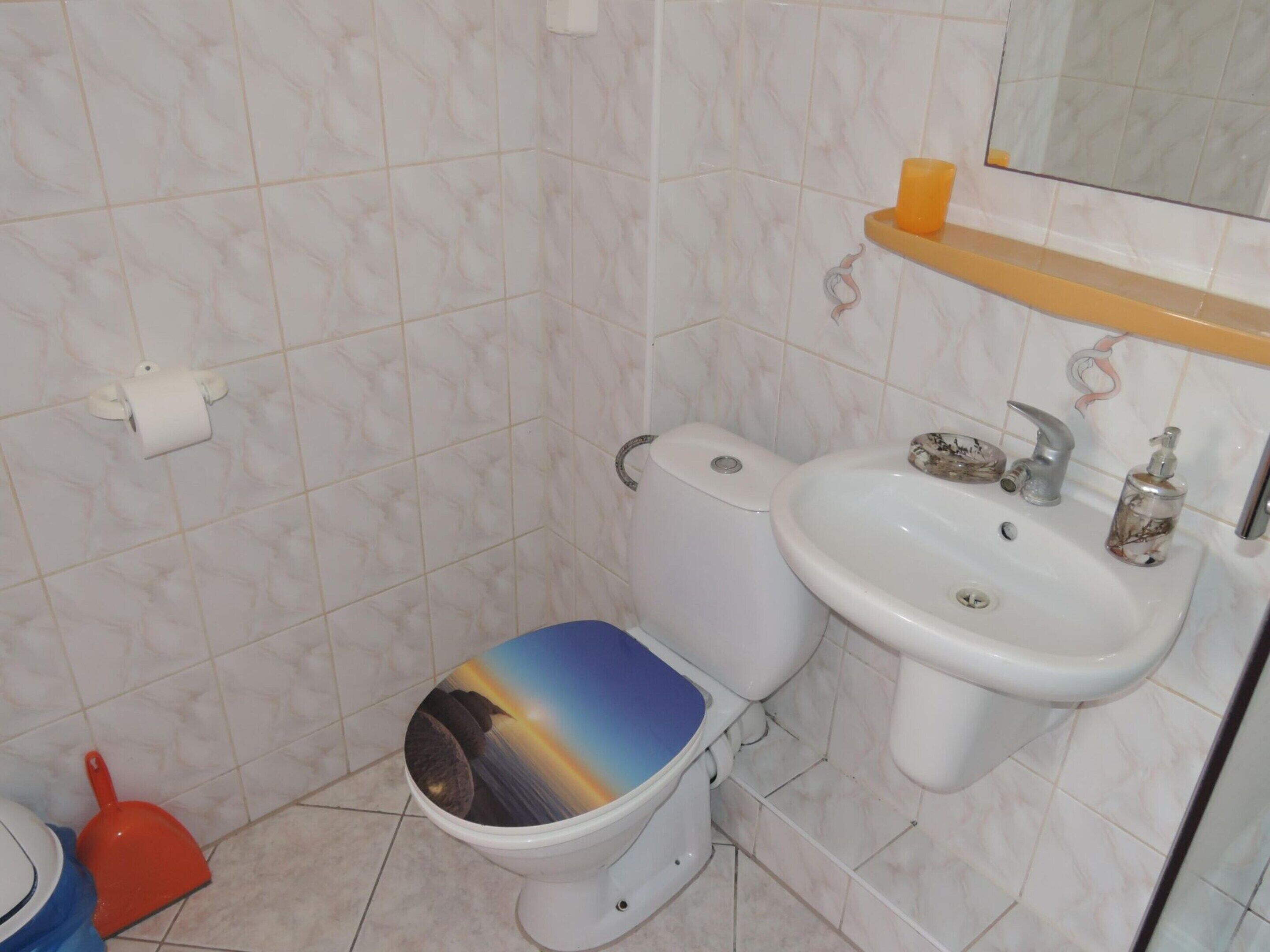 Un baño con inodoro, lavabo y estante sobre el lavabo.