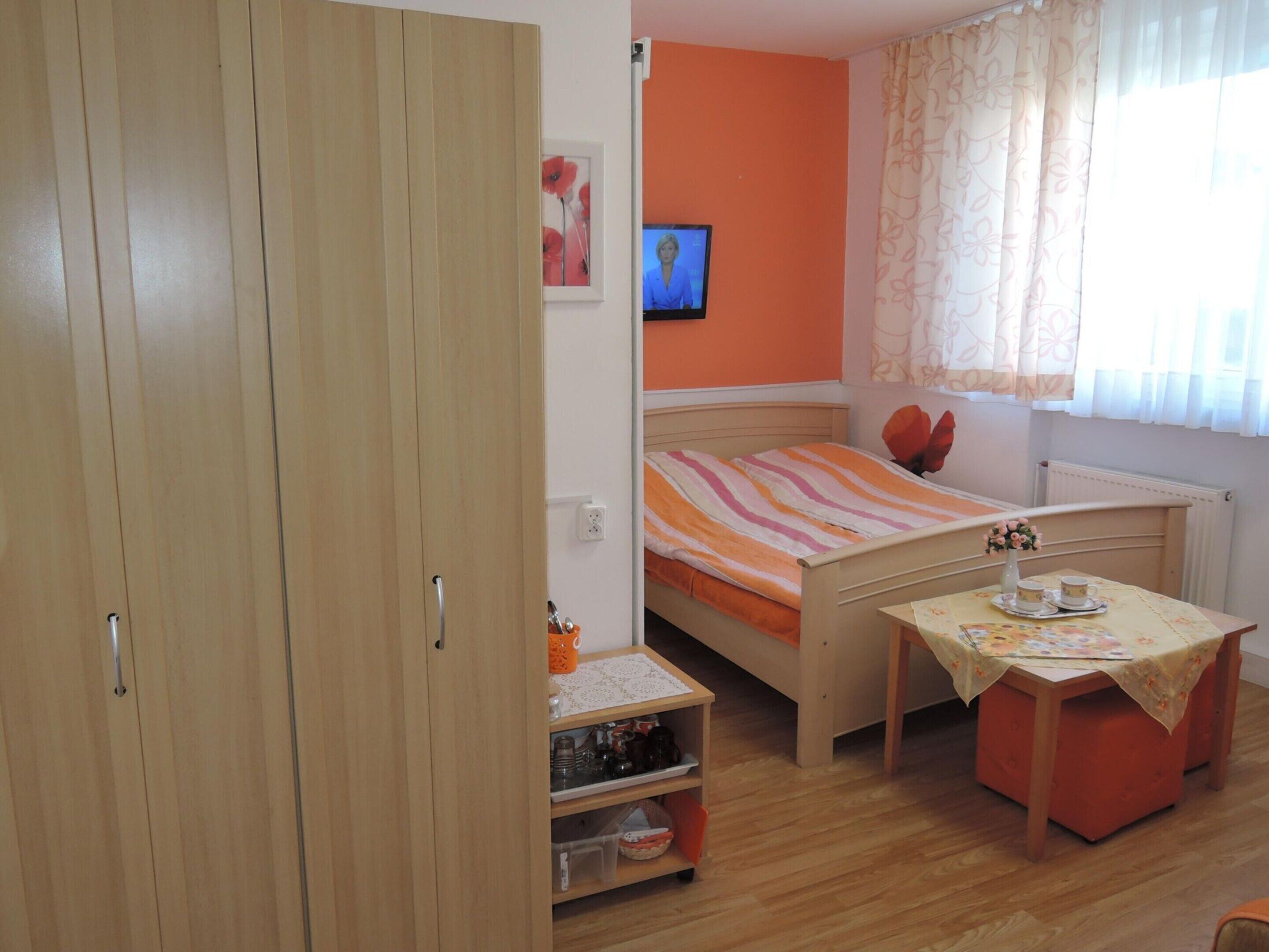 A bedroom with a bed, a small table with cups, a cabinet, and a TV on the wall.