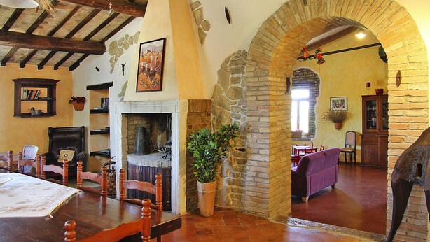 Un coin repas rustique avec une table et des chaises en bois, une cheminée et une arche en pierre menant à une autre pièce.