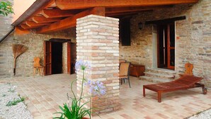 Un bâtiment en pierre agrémenté d’une pergola en bois, d’un pilier en briques et d’un fauteuil de jardin en bois.