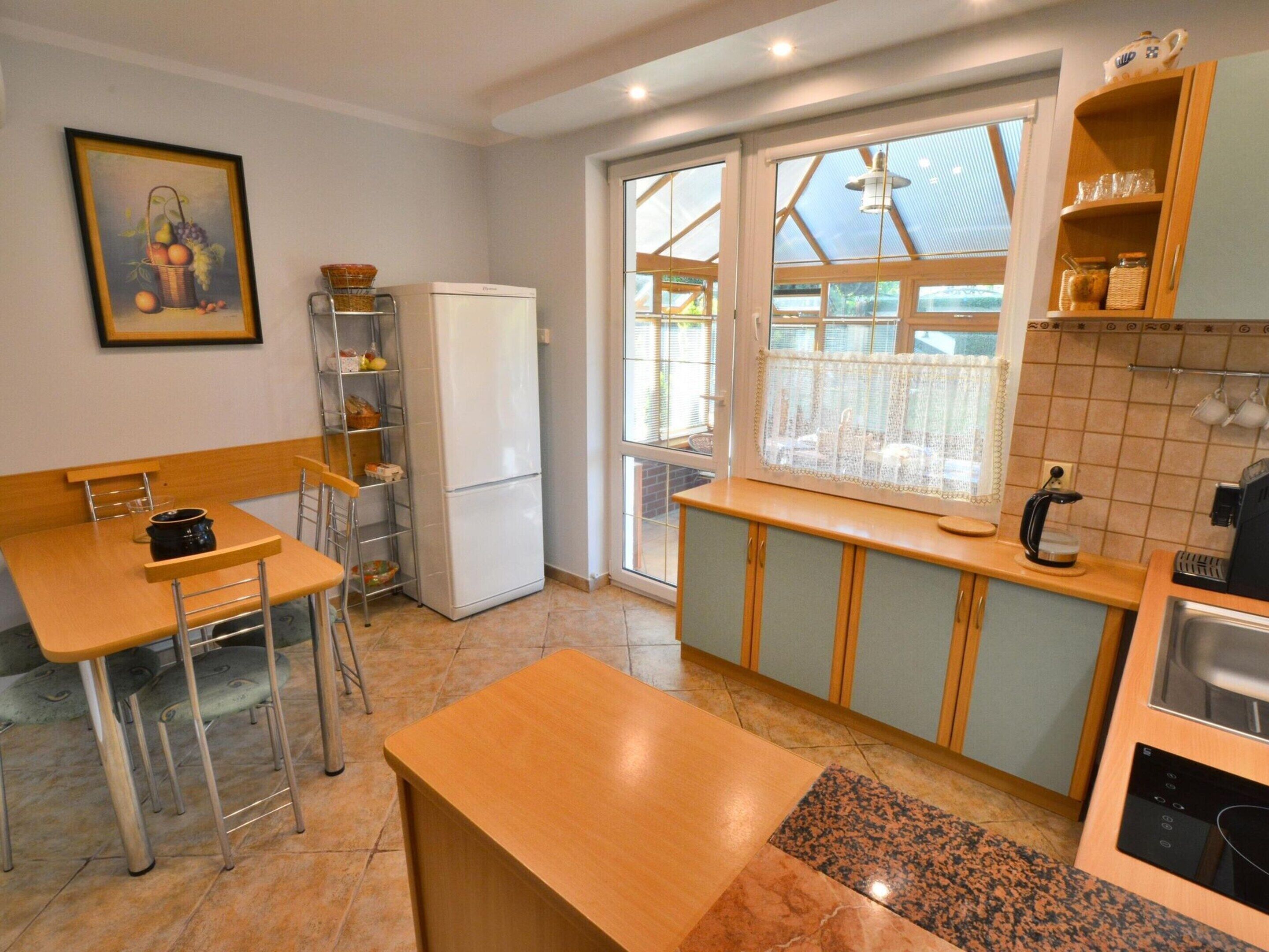 A compact kitchen with a refrigerator, a sink, a coffee maker, and a dining area with a chair and table.