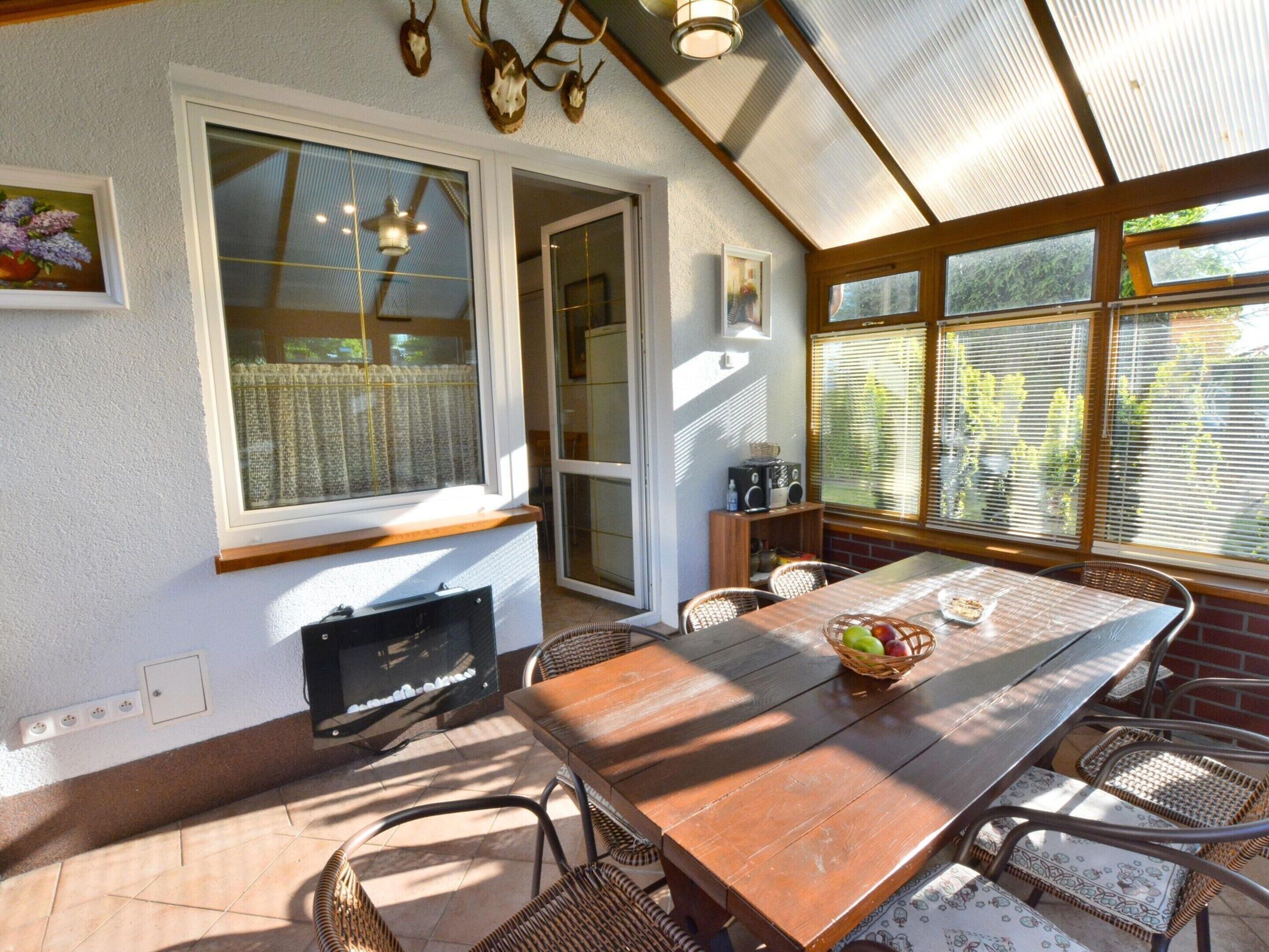 A sunlit patio with a wooden table, wicker chairs, and a television.