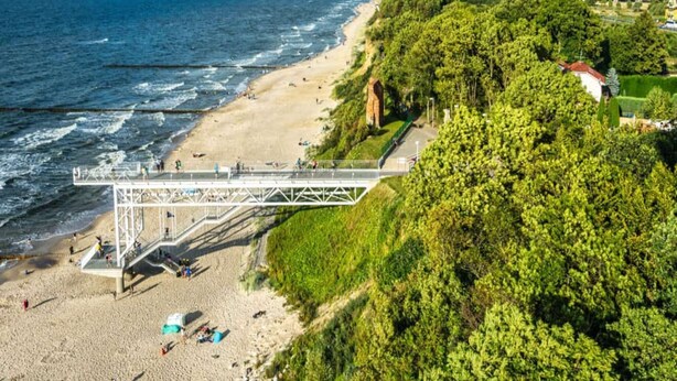 Une plage avec un pont piétonnier, une rive sablonneuse et de la végétation.