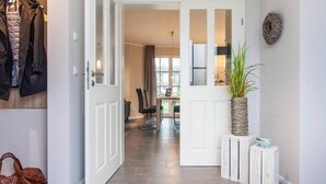 A hallway with a coat rack, a potted plant, and a dining area visible through the door. - Komfortables Ferienhaus mit Sauna in Fuhlendorf (Fuhlendorf)