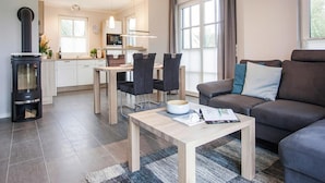 A modern living room with a sofa, a coffee table, and a dining area with chairs and a table. - Komfortables Ferienhaus mit Sauna in Fuhlendorf (Fuhlendorf)