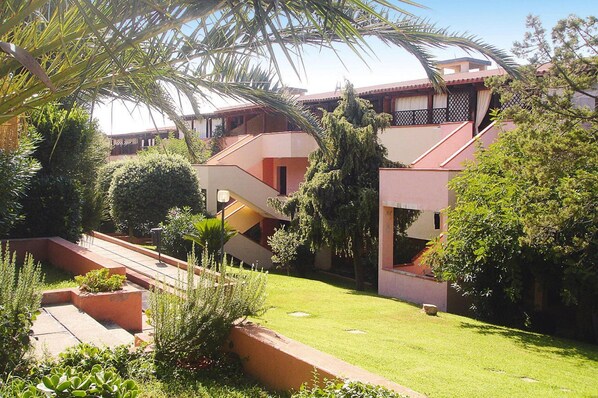 A courtyard with a central staircase, surrounded by lush greenery and buildings with balconies. - Apartment in Porto Rotondo Near Sandy Beach (Olbia)