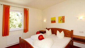 Een slaapkamer met een houten bed, wit beddengoed, oranje gordijnen en twee wandlampen.