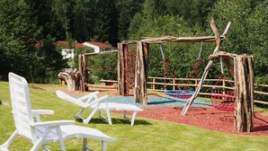 Ein Spielplatz mit Schaukeln und Rutschen, umgeben von einem Holzzaun und Bäumen.