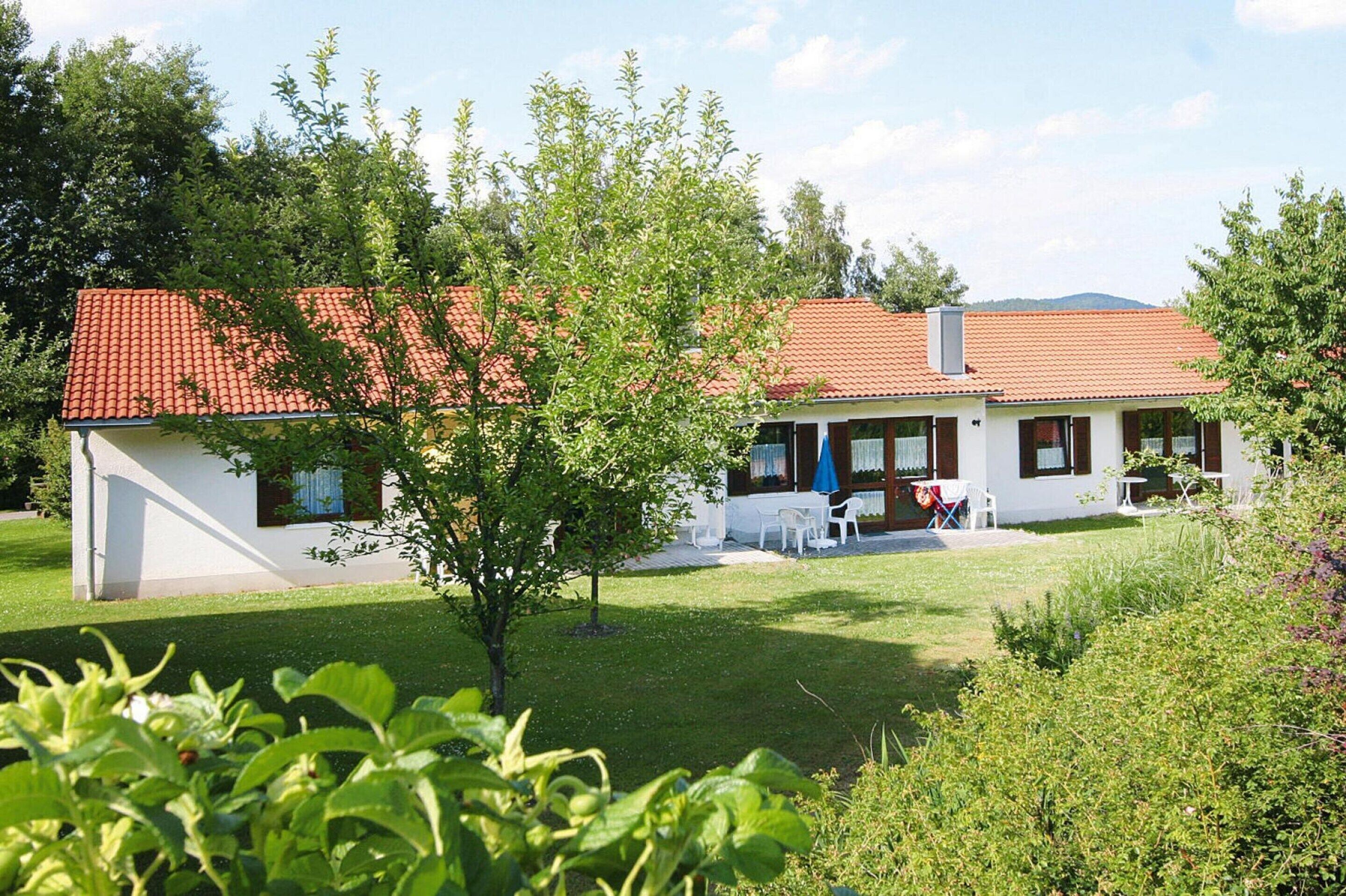Une maison à deux étages, avec un toit recouvert de tuiles rouges, un petit jardin et un espace extérieur aménagé pour s’asseoir.