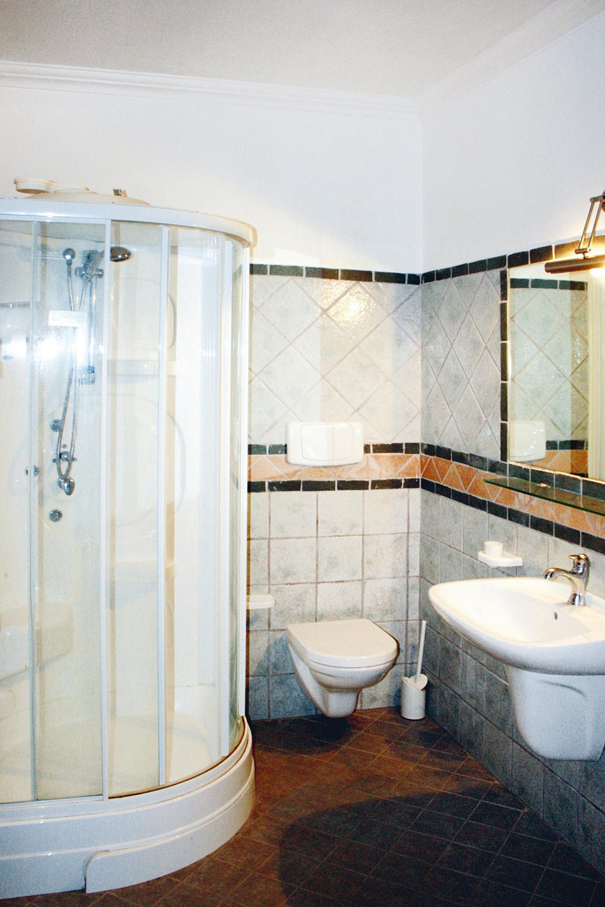 Un baño con ducha de vidrio, inodoro, lavamanos y espejo.
