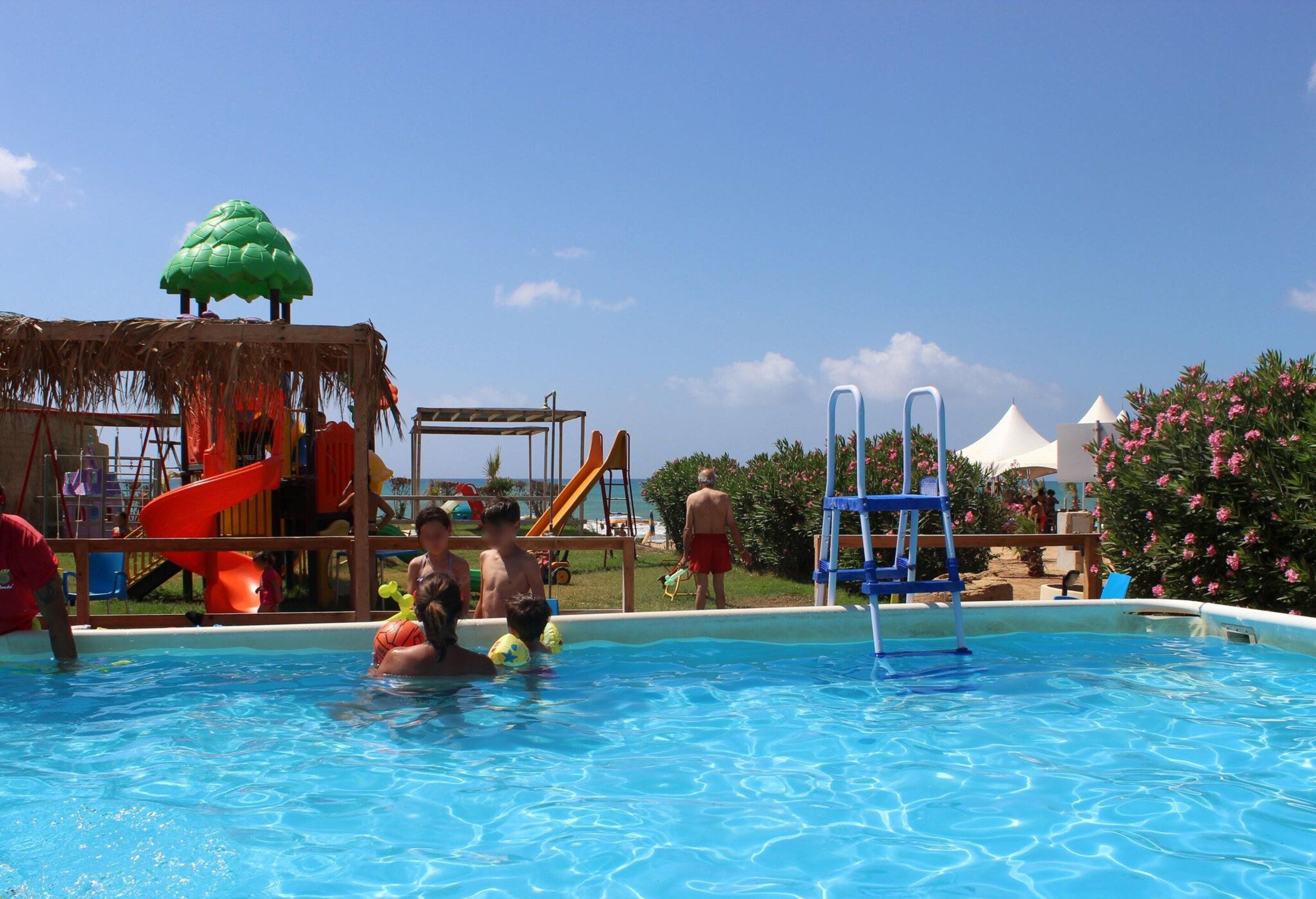 A swimming pool with a slide and play structures, surrounded by a clear sky.