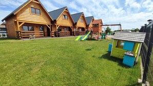 A wooden cabin-style building with a grassy yard and a playground. - Family Resort in Niechorze Near Lighthouse (Rewal)