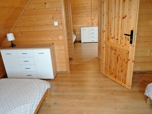 A room with a sloped ceiling, wooden walls, a bed with patterned bedding, a bedside table with a lamp, and a small white cabinet. - Family Resort in Niechorze Near Lighthouse (Rewal)
