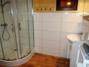 A bathroom with a glass-enclosed shower, a white sink, and a wooden floor. - Family Resort in Niechorze Near Lighthouse (Rewal)