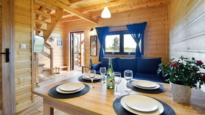 A wooden cabin interior with a dining table set for four, a sofa, and a window with curtains. - Family Resort in Niechorze Near Lighthouse (Rewal)