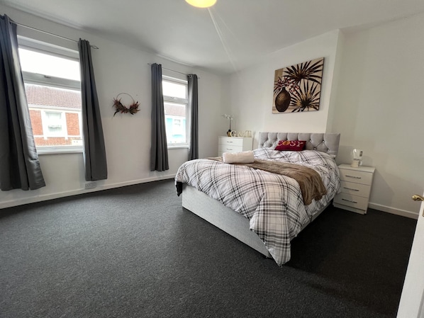 A bedroom with a bed, a nightstand, a wall-mounted artwork, and a window with curtains.