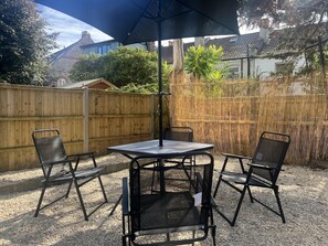 An outdoor patio with a table and four chairs, a large umbrella, and a bamboo fence.