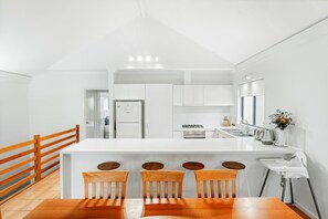 A modern kitchen with white cabinets, a central island with bar stools, and a wooden dining table.