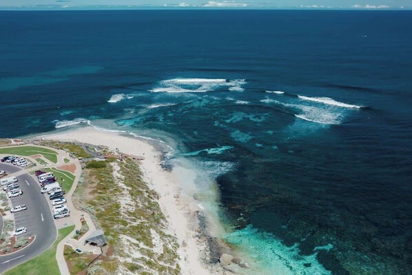 An aerial view of a coastal area with a parking lot, beach, and ocean.