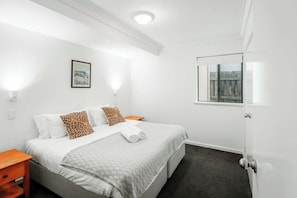 Une chambre d’hôtel avec un lit, une table de chevet, un tableau encadré au mur et une fenêtre donnant sur un paysage.