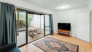 A living room with a sliding glass door, a flat-screen TV, a wooden bench, and a patterned rug.