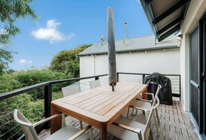 A wooden deck with a table and chairs, a barbecue grill, and a covered grill area.