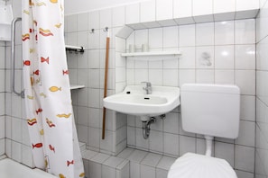 Et badeværelse med hvid vask, toilet og bruseforhæng med fiskemønster.