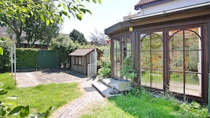 A house with a large glass conservatory, a brick garage, and a paved backyard. - A Holiday Home in Busum With a Barbecue (Büsum)