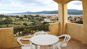 Ein Balkon mit Tisch und Stühlen, mit Blick auf eine Küstenstadt, Gebäude und Berge in der Ferne.