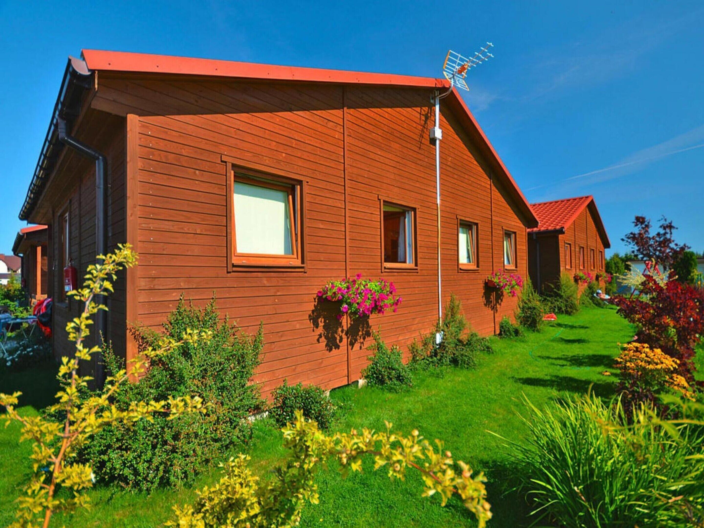 A wooden house with a red roof, multiple windows, and a garden with various plants and flowers.