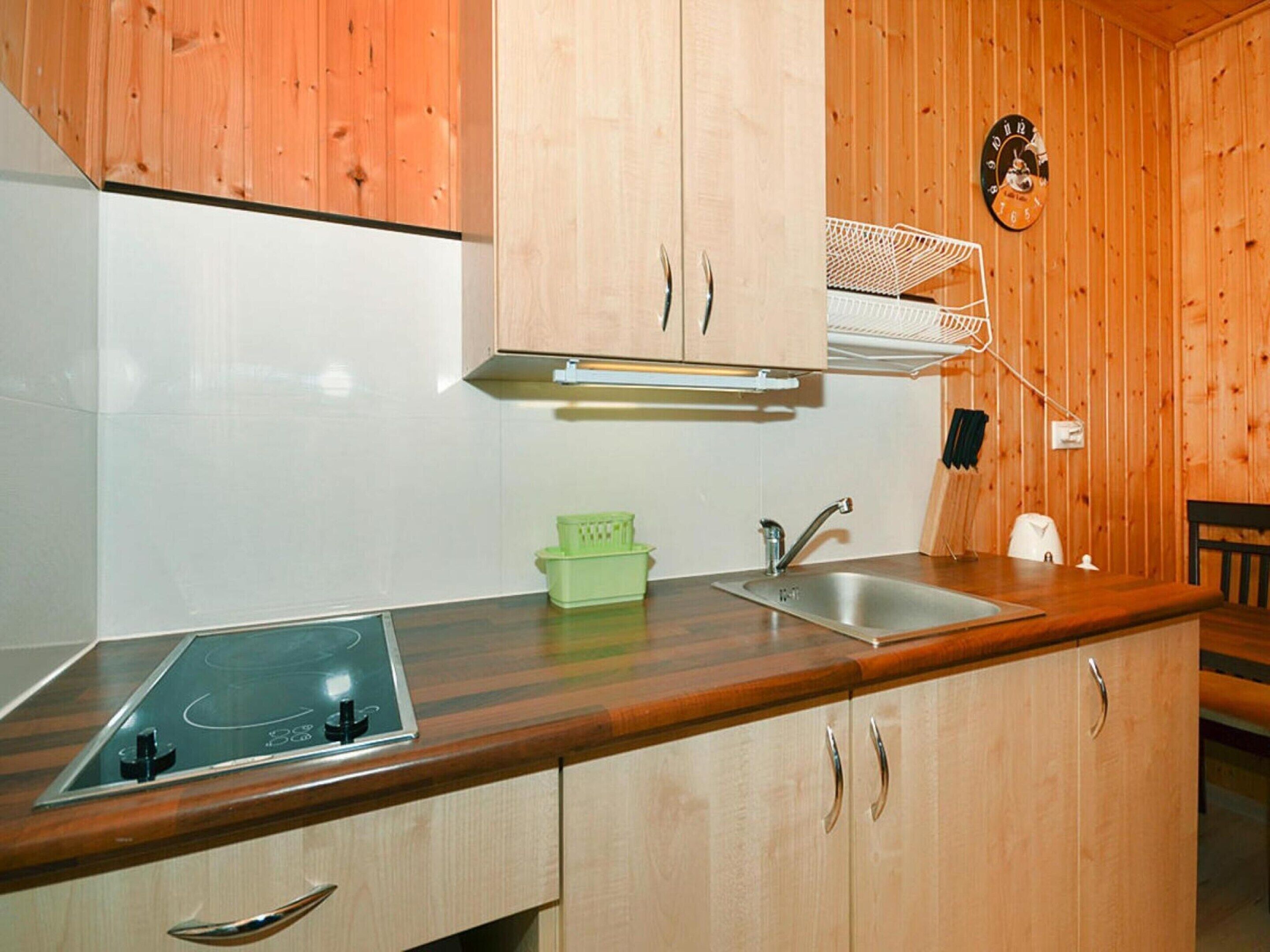 Une cuisine avec des meubles de rangement en bois, un évier, une cuisinière et un étagère fixée au mur.