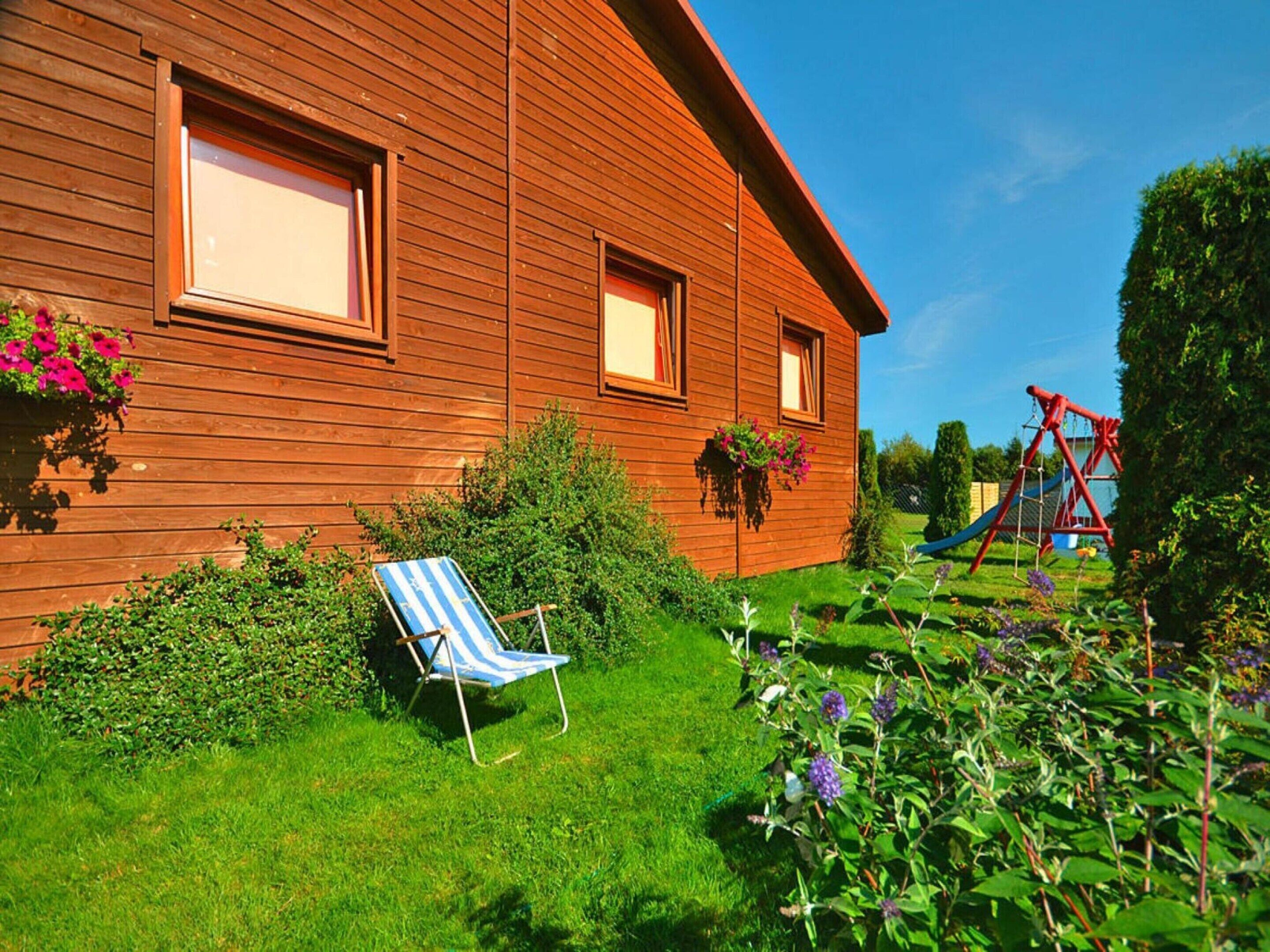 A wooden house with a garden, a swing set, and a blue and white striped chair.