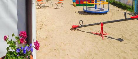 A playground with swings, a slide, and a seesaw on sandy ground.